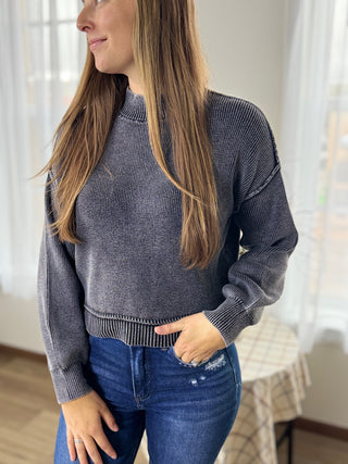 Woman wearing a gray sweater and blue jeans indoors.