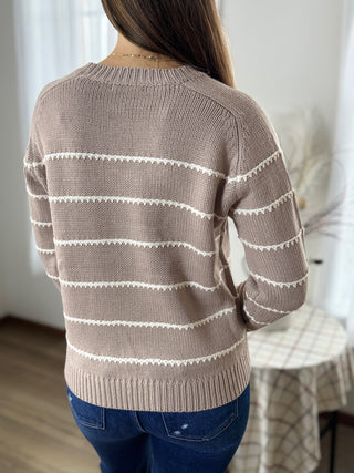 Person wearing a beige sweater with white stripes indoors