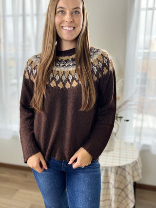 Woman wearing a brown sweater with a patterned design, standing indoors.