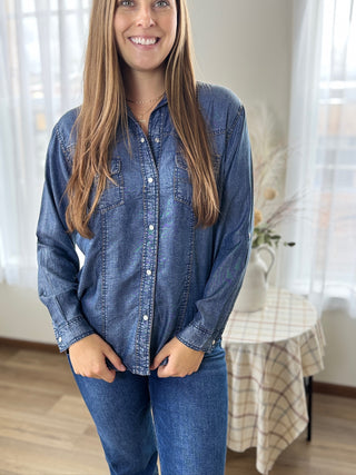 Woman wearing a blue denim shirt and jeans indoors.