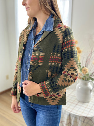 Person wearing a green patterned jacket with a denim collar indoors.