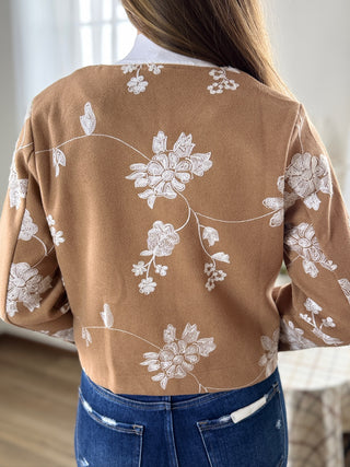 Brown sweater with white floral embroidery worn by a person, blurred background