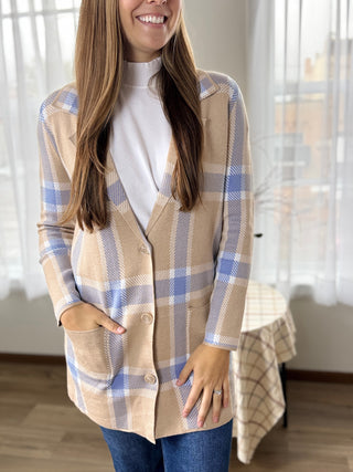 Woman wearing a plaid shirt in a room with curtains and a bed.
