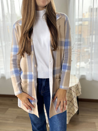 Person wearing a beige and blue plaid cardigan over a white shirt and jeans indoors.