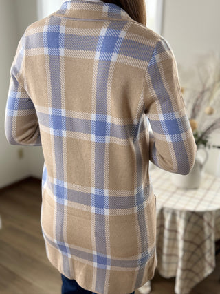 Person wearing a beige and blue plaid shirt in a room with a table and chair.