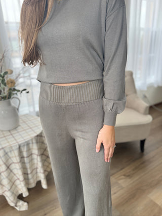 Person wearing a gray outfit in a room with a table and chair.