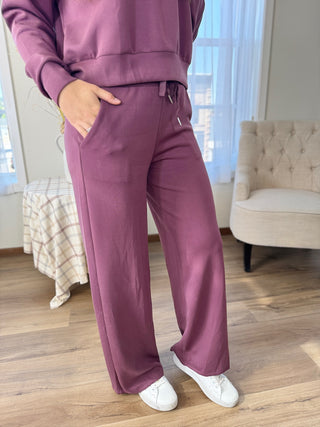 Person wearing a purple tracksuit in a room with wooden flooring and a beige chair.