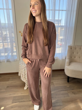 Woman wearing a brown tracksuit in a room with large windows.