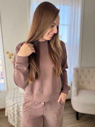 Woman wearing a brown tracksuit in a room with a couch and window.