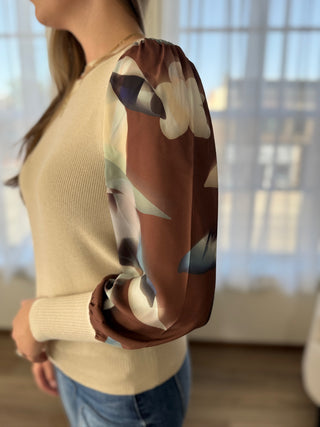 Person wearing a beige sweater with a brown sleeve featuring a floral pattern.