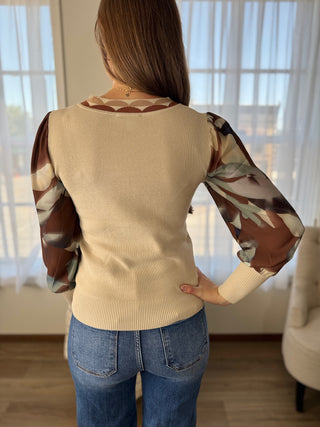 Person wearing a beige sweater with floral sleeves in a room with large windows.