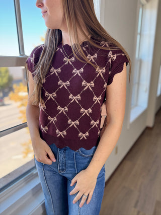 Person wearing a maroon sweater with bow pattern and blue jeans indoors.