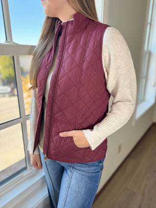 Person wearing a maroon quilted vest indoors near a window