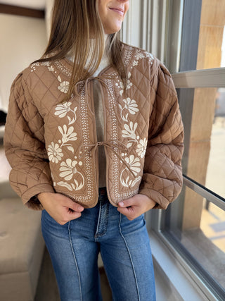 Photo of a woman in a tan quilted jacket with embroidery.