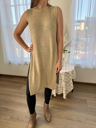 Person wearing a beige sleeveless dress in a room with a table and curtains.
