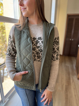Woman wearing a green quilted vest over a patterned sweater indoors.