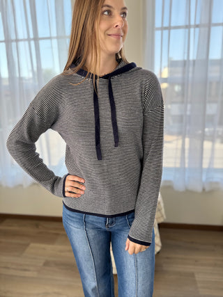 Woman wearing a striped hoodie and jeans indoors with light curtains in the background