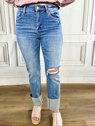 Person wearing light blue jeans with a distressed knee on a wooden floor.
