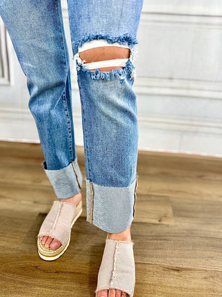 Close-up of blue jeans with a distressed knee on a wooden floor.