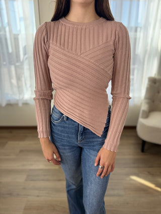 Person wearing a ribbed pink sweater and blue jeans indoors.