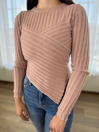 Person wearing a ribbed pink sweater and blue jeans indoors.