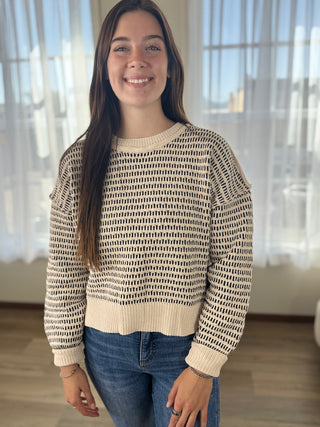 Woman wearing a patterned sweater and jeans indoors with a blurred background
