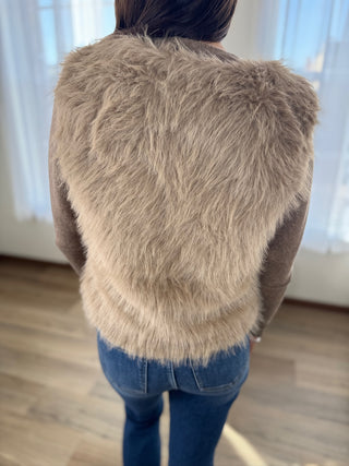 Person wearing a fluffy beige jacket in a room with light-colored walls.