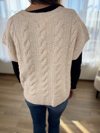Person wearing a beige cable knit sweater with a blurred background