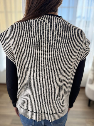 Person wearing a black and white striped sweater in a room with light-colored walls.