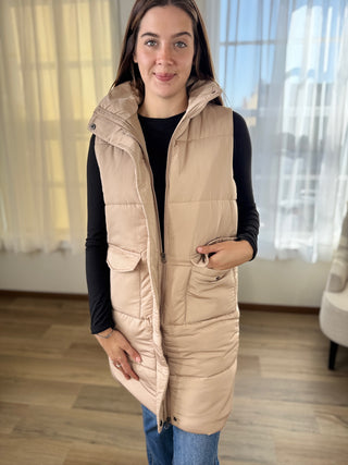 Woman wearing a beige puffer vest indoors with curtains in the background