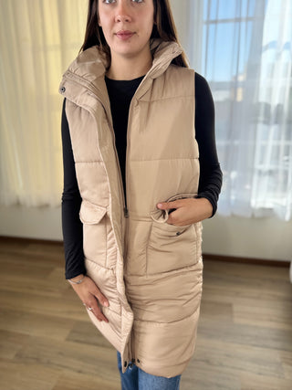 Woman wearing a beige puffer vest indoors with a neutral background