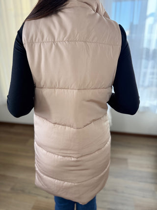 Person wearing a beige puffer vest over a dark long-sleeve shirt indoors.