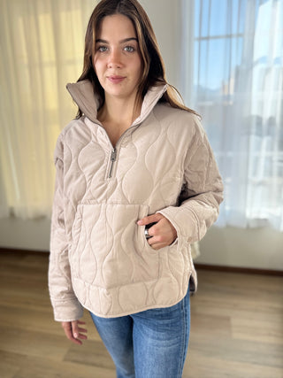 Woman wearing a beige quilted jacket indoors with a neutral background