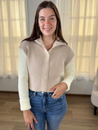 Woman wearing a beige ribbed sweater and blue jeans indoors.