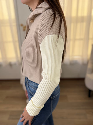 Person wearing a beige and white ribbed sweater with a blurred background