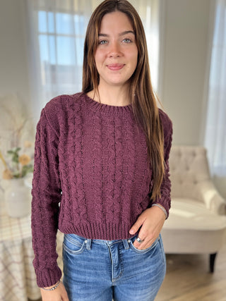 Woman wearing a purple sweater and blue jeans indoors.