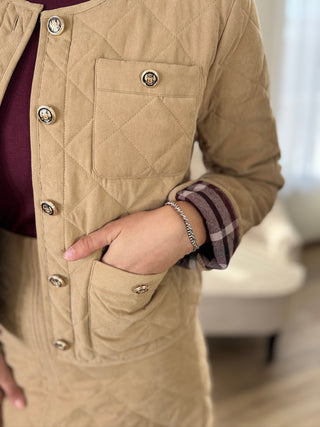 Close-up of a person wearing a beige quilted jacket with a blurred indoor background