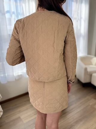 Person wearing a beige quilted jacket and skirt set indoors.