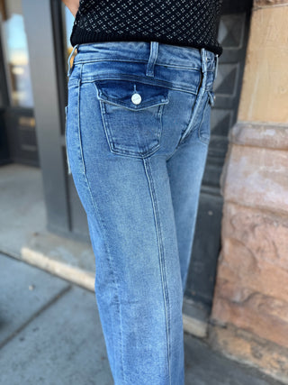 Close-up of a person wearing light blue denim jeans with a black patterned top, standing outdoors near a storefront.