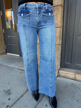 A person wearing light blue wide-leg denim jeans with a raw hem, paired with black pointed-toe boots, standing outdoors on a sidewalk in front of a building.