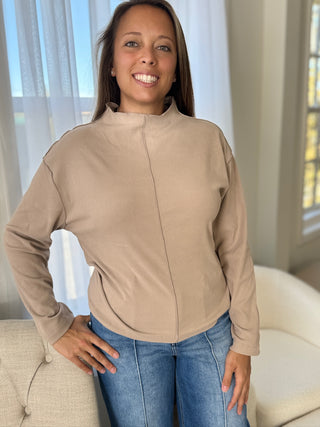 Woman wearing a beige jacket and blue jeans indoors