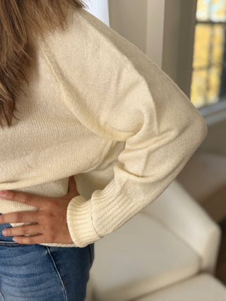 Person wearing a cream sweater and blue jeans indoors.