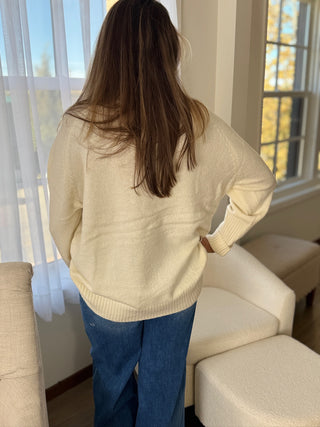 Person wearing a beige sweater and blue jeans standing in a living room.
