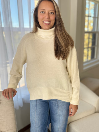 Woman wearing a beige sweater and blue jeans indoors.
