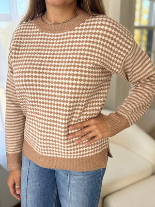 Person wearing a brown and white patterned sweater with blue jeans indoors.