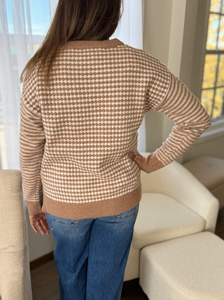Person wearing a brown and white checkered sweater and blue jeans in a living room.