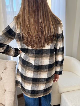 Person wearing a plaid shirt in a room with light-colored walls and furniture.