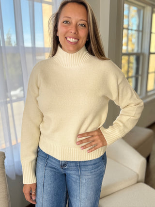 Woman wearing a cream sweater and blue jeans indoors