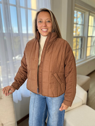 Woman wearing a brown quilted jacket in a bright living room.