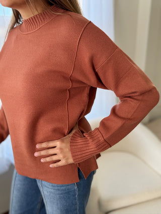 Person wearing a brown sweater and blue jeans with a blurred background